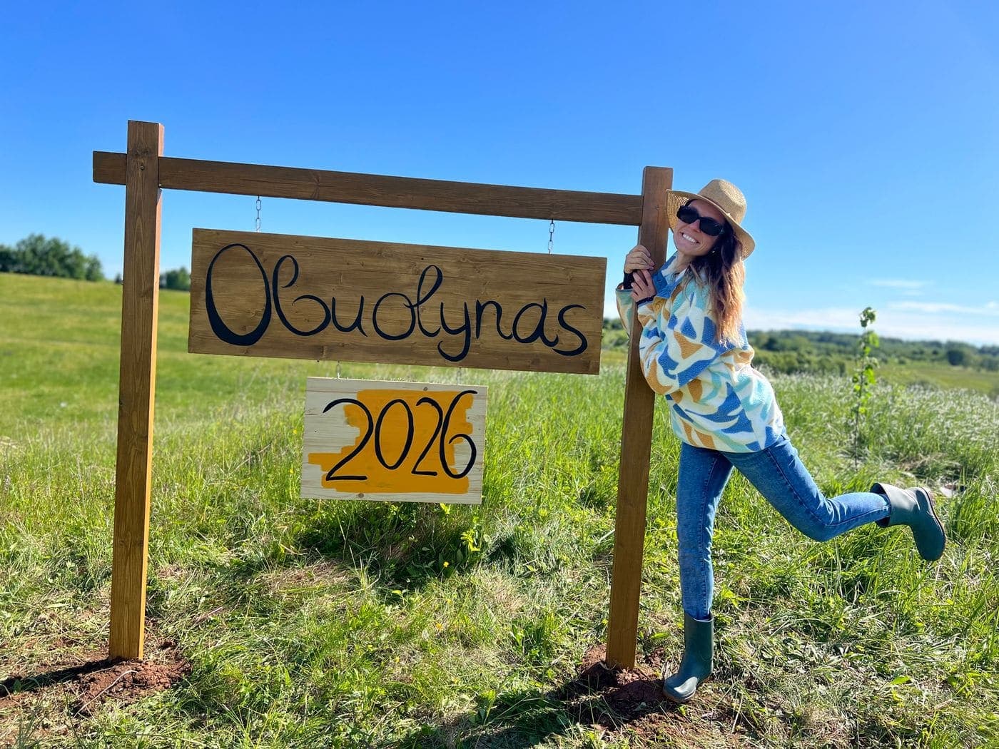 Gytė prie medinio Obuolyno ženklo sode Molėtų kalvose