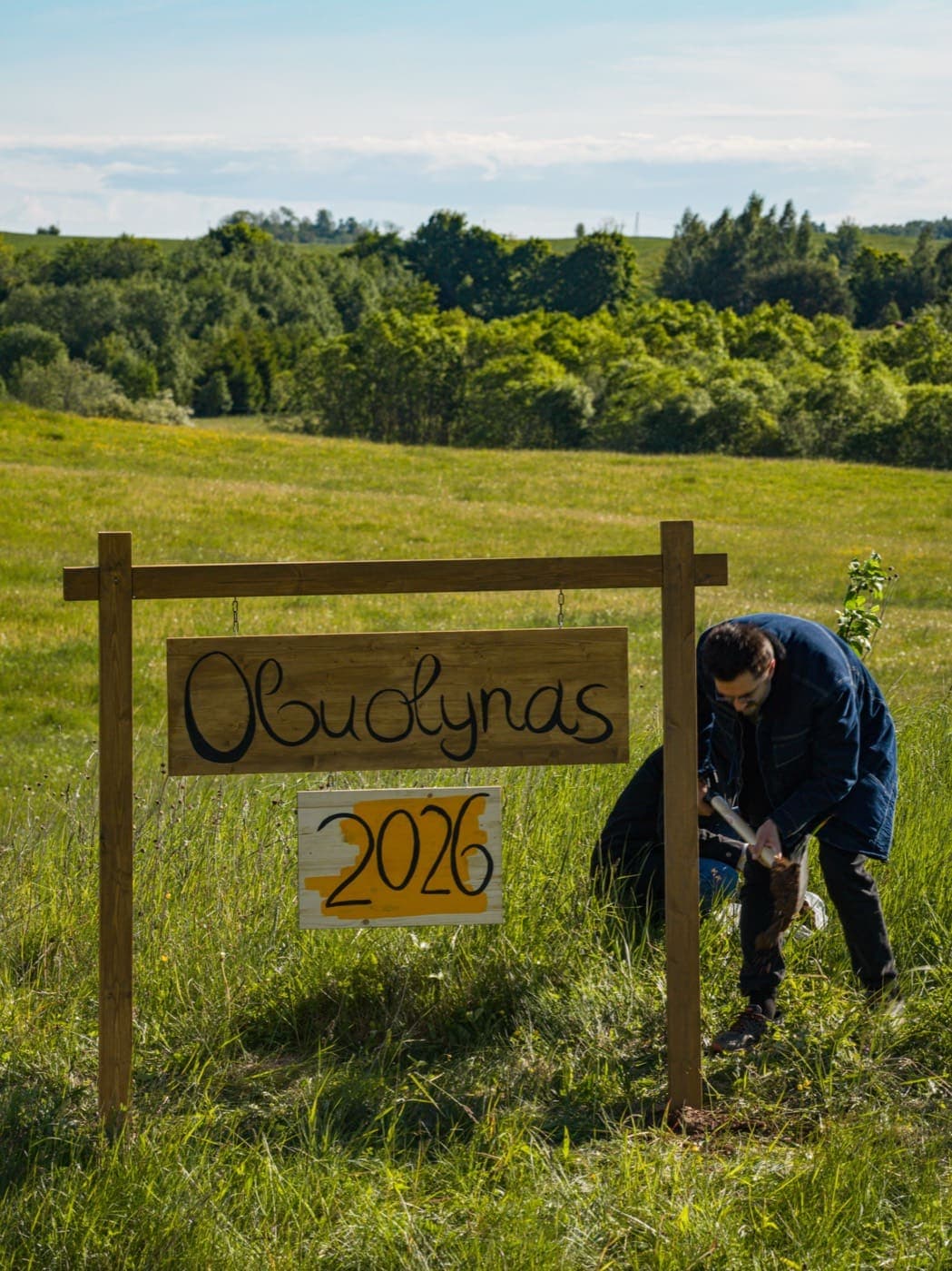 Andrius sodina pirmąją Obelį prie medinio ženklo „Obuolynas 2026“